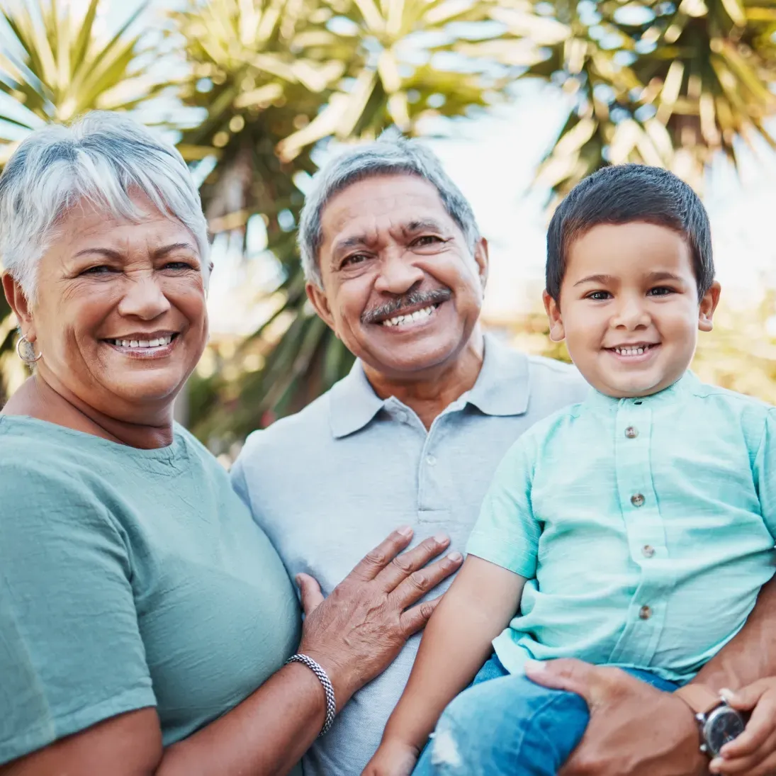 Older couple and their grandson at the camera, with the man holding the boy in his arms