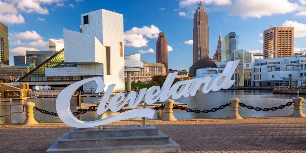 Cleveland skyline with the word "Cleveland" in front of it, surrounded by buildings, trees, poles, and a fence