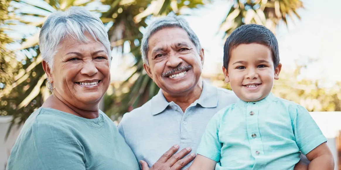 Older couple and their grandson at the camera, with a tree in the background and a wall behind them