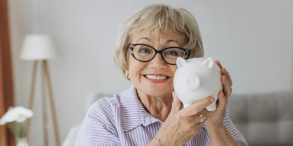 Older woman with a warm smile on her face, holding a piggy bank in her hands