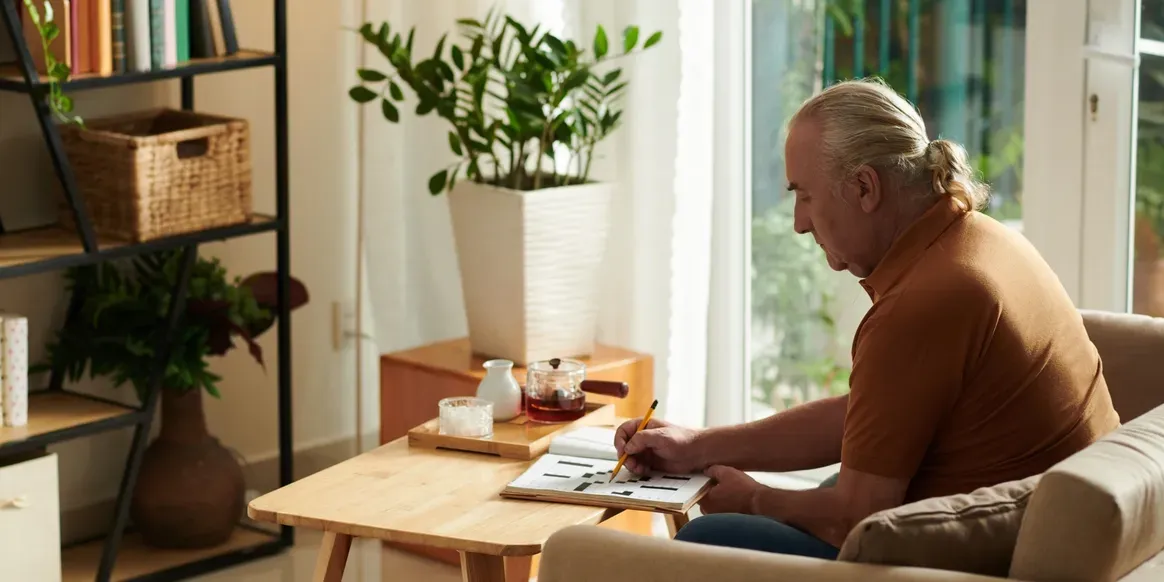 Man sitting on a couch in his living room, writing on a piece of paper with a pen
