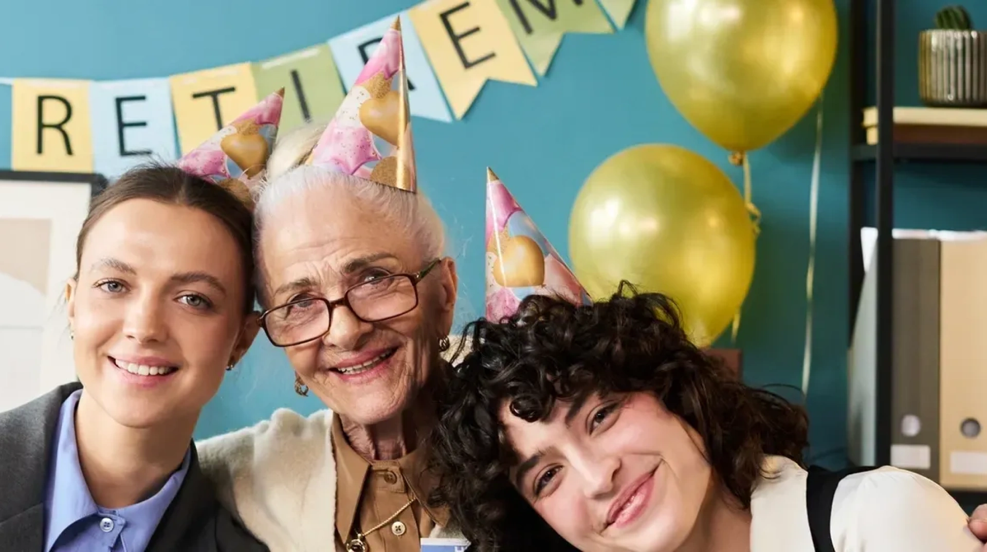 Three women wearing party hats and for a photo in front of a wall decorated with balloons, a photo frame