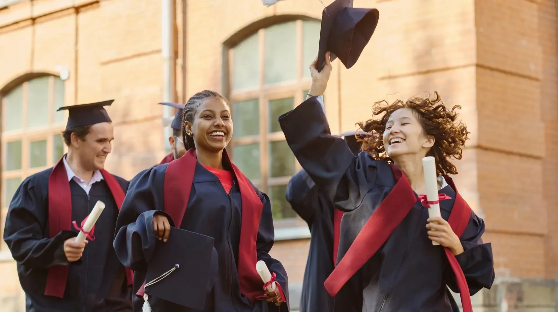 Group of people in graduation robes and hats, and holding diplomas in their hands, standing in front of a building