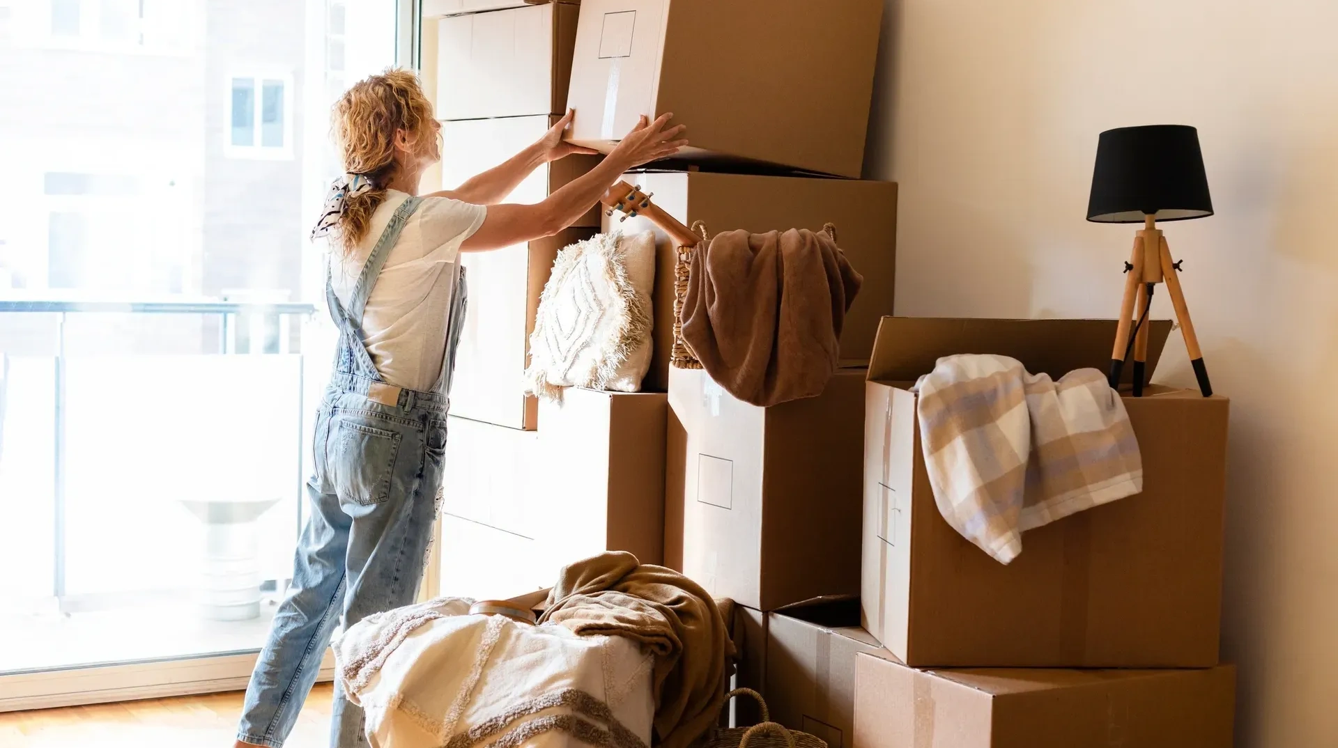 Woman standing in front of a pile of moving boxes, holding a cardboard box in her hands