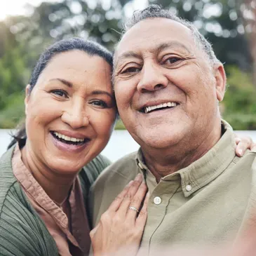 Older couple at the camera, surrounded by trees and a blurred background